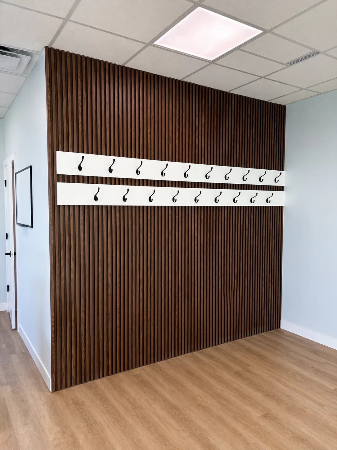 Dark slatted wall with white hook rail in mudroom