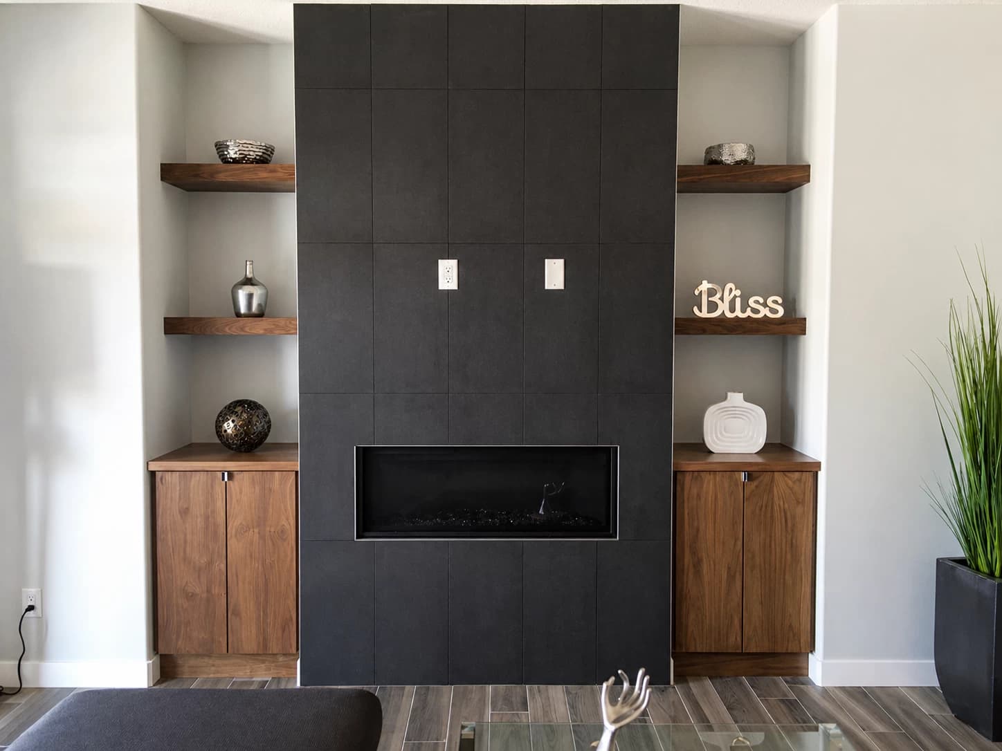 Built-in cabinetry flanking a black tile linear fireplace with walnut floating shelves