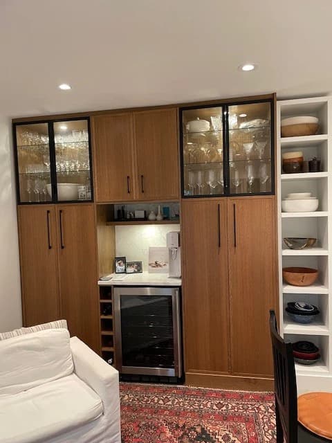 Light oak dry bar with glass-front upper cabinets and built-in beverage fridge